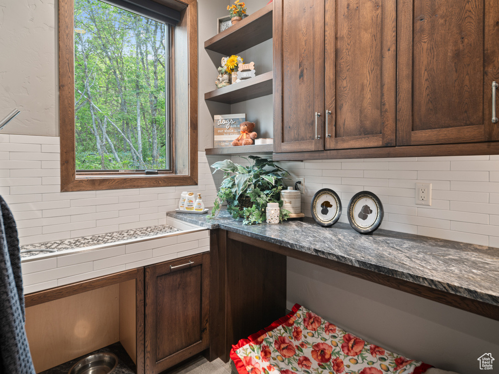Kitchen with open shelves, backsplash, dark brown cabinets, and dark stone countertops
