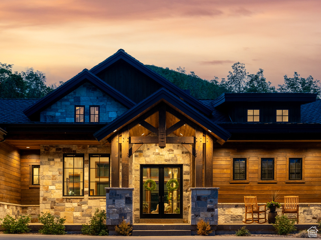 View of front facade with stone siding, french doors, covered porch, and a shingled roof