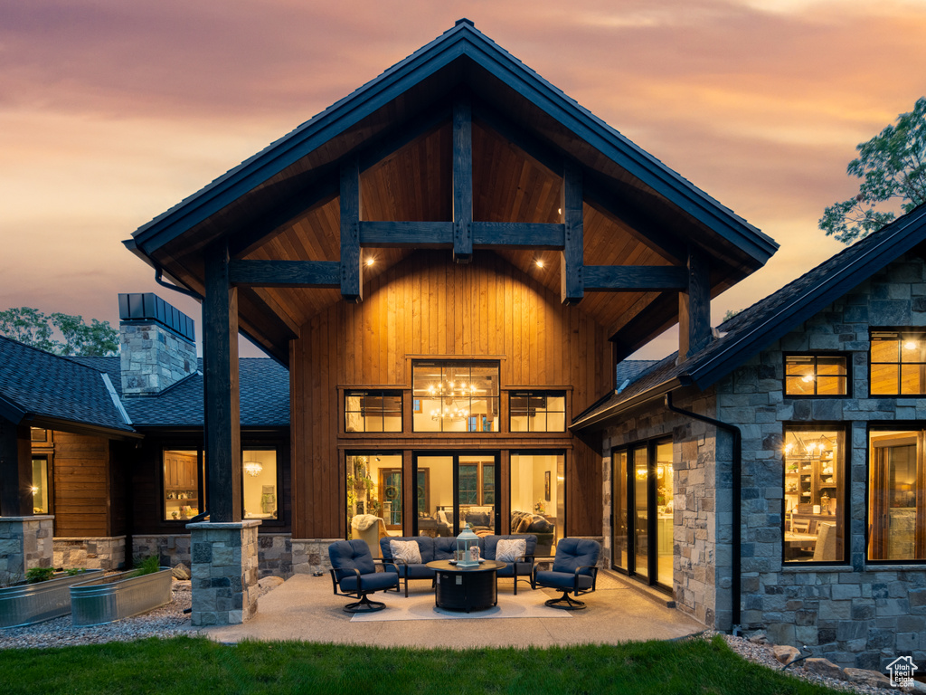 Back of house with an outdoor living space, stone siding, a patio, roof with shingles, and a chimney
