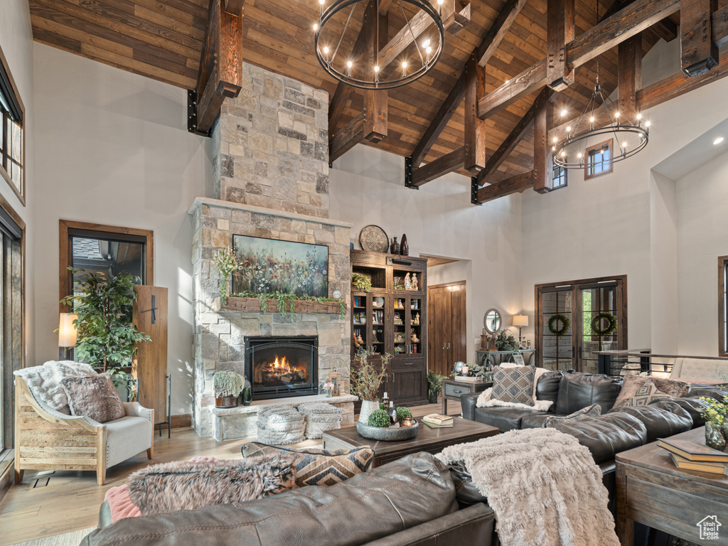 Living area with high vaulted ceiling, wooden ceiling with exposed beams, a chandelier, hardwood / wood-style flooring, and a stone fireplace