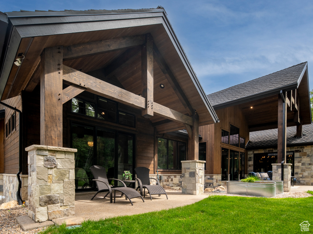 Rear view of house with stone siding, roof with shingles, and a patio area