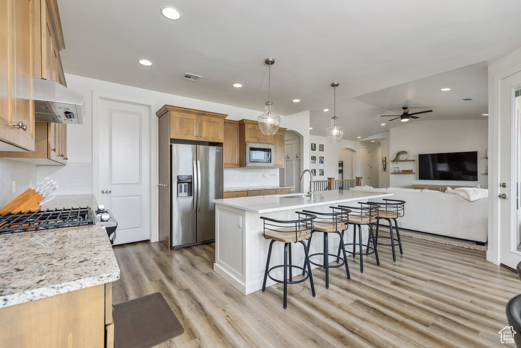 Kitchen featuring appliances with stainless steel finishes, arched walkways, ventilation hood, a breakfast bar, and recessed lighting