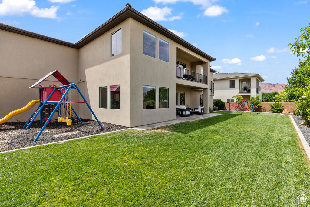 Back of property with a playground, stucco siding, a balcony, and a patio