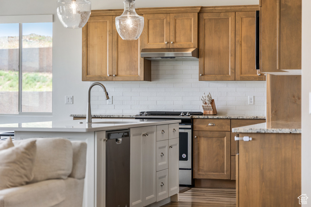 Kitchen with gas range, under cabinet range hood, tasteful backsplash, and brown cabinetry