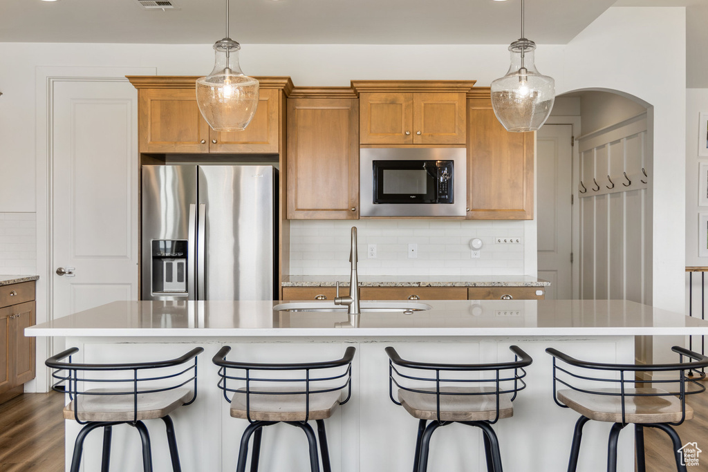 Kitchen featuring appliances with stainless steel finishes, light countertops, brown cabinets, tasteful backsplash, and a sink