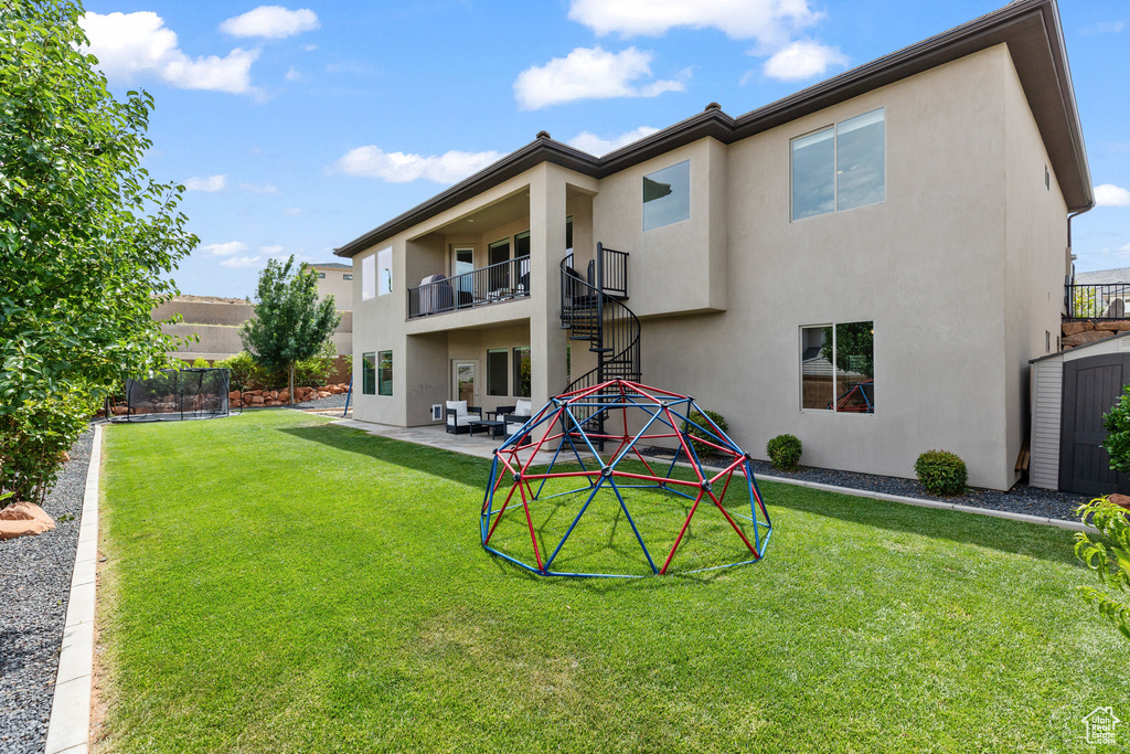 Rear view of house with stucco siding, a trampoline, a patio, and a balcony
