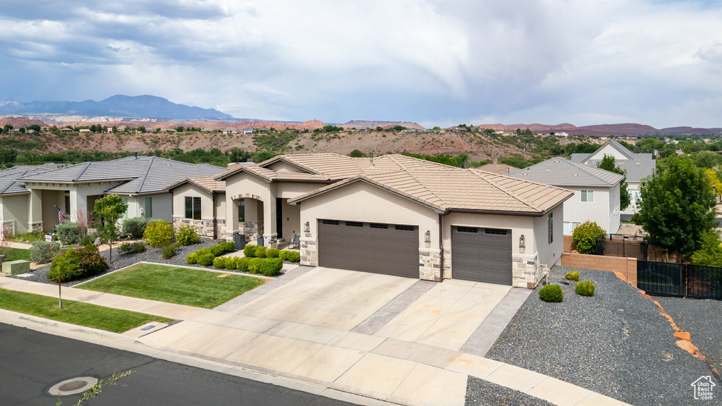 View of front of property featuring an attached garage, stucco siding, concrete driveway, a mountain view, and stone siding