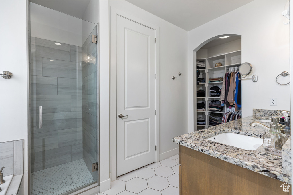 Bathroom with a shower stall, a spacious closet, double vanity, tile patterned flooring, and baseboards