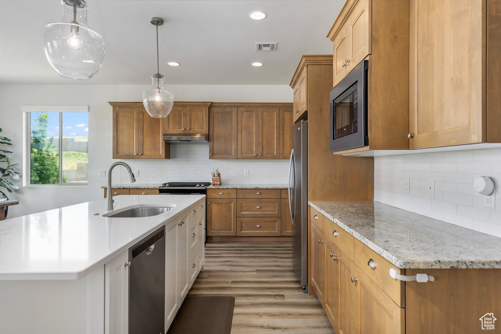 Kitchen with stainless steel appliances, a sink, under cabinet range hood, tasteful backsplash, and a kitchen island with sink