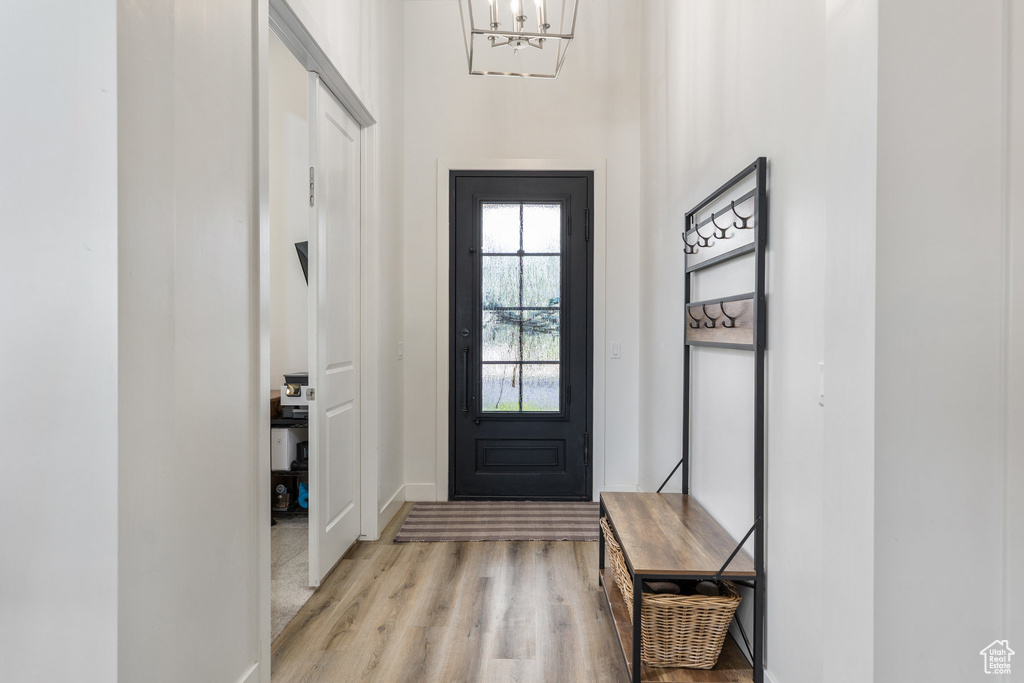 Entryway with light wood finished floors, a chandelier, and baseboards
