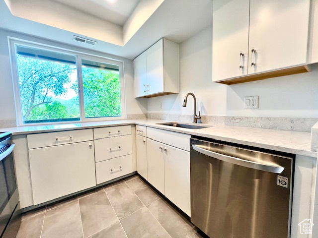Kitchen with dishwasher, a sink, white cabinetry, light tile patterned floors, and light stone countertops