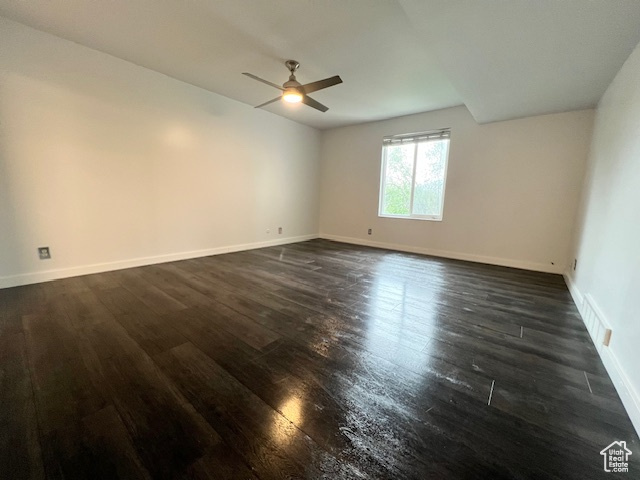 Empty room with dark wood finished floors, ceiling fan, and baseboards