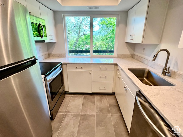 Kitchen with stainless steel appliances, a sink, light tile patterned floors, white cabinetry, and a raised ceiling