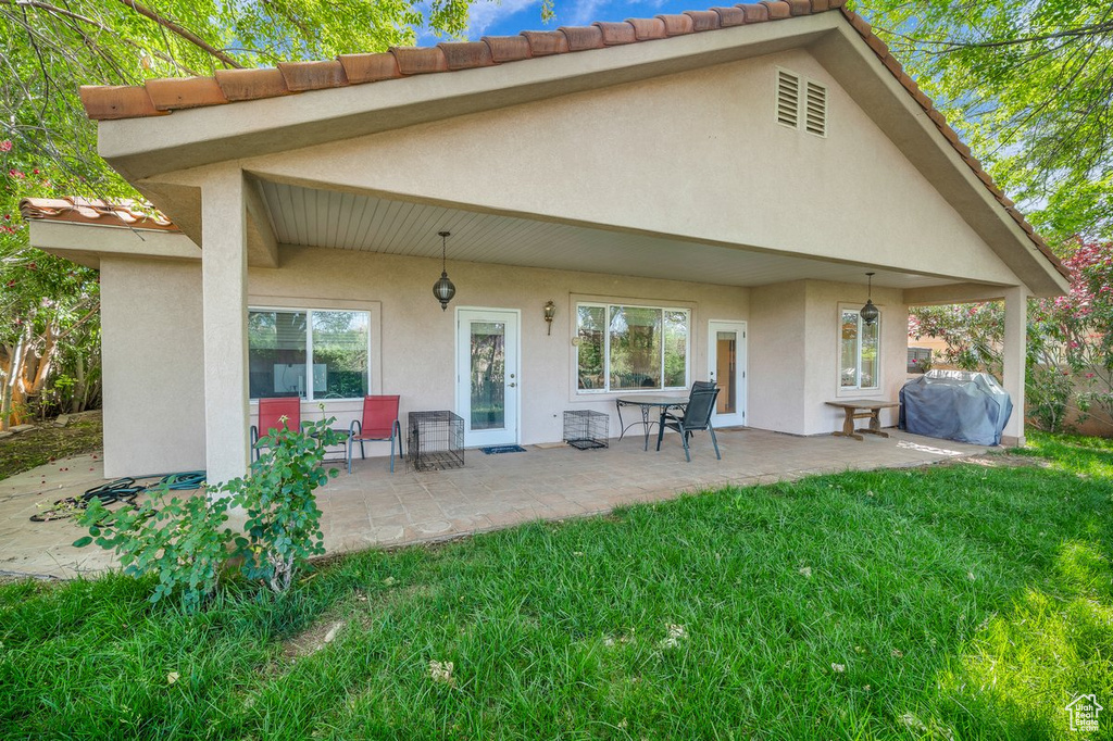 Rear view of house featuring stucco siding, a lawn, and a patio