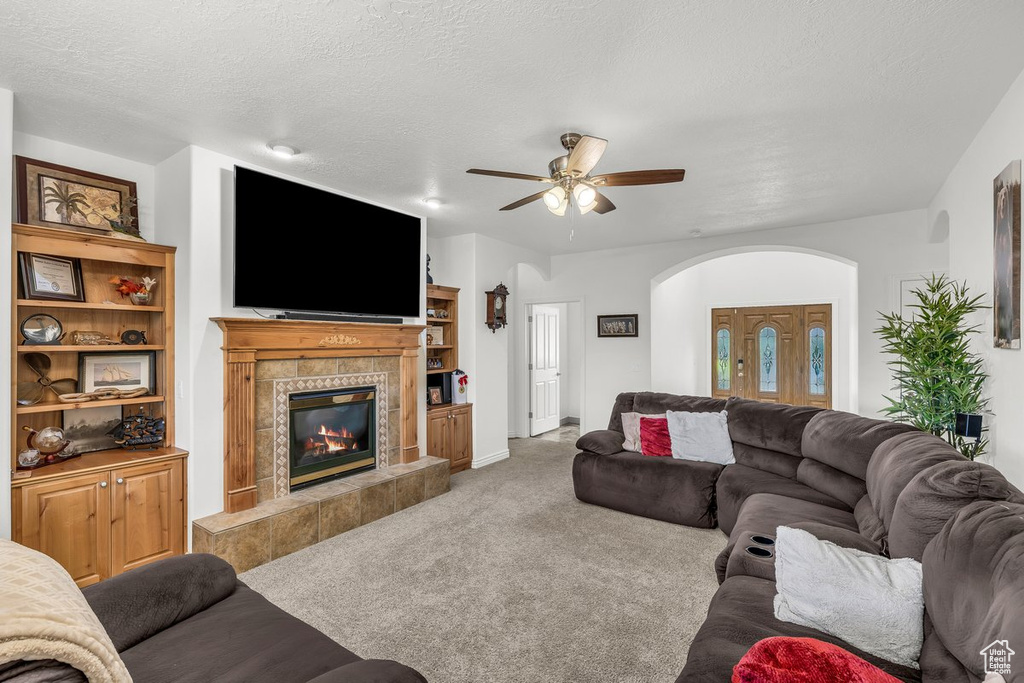 Living room with arched walkways, a tiled fireplace, carpet flooring, a ceiling fan, and a textured ceiling