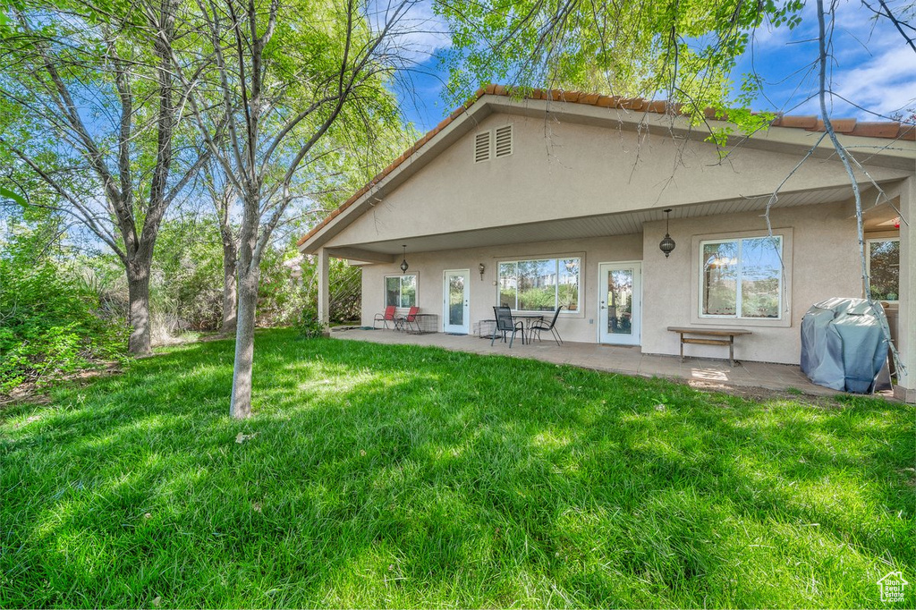 Rear view of house with stucco siding, a lawn, and a patio area
