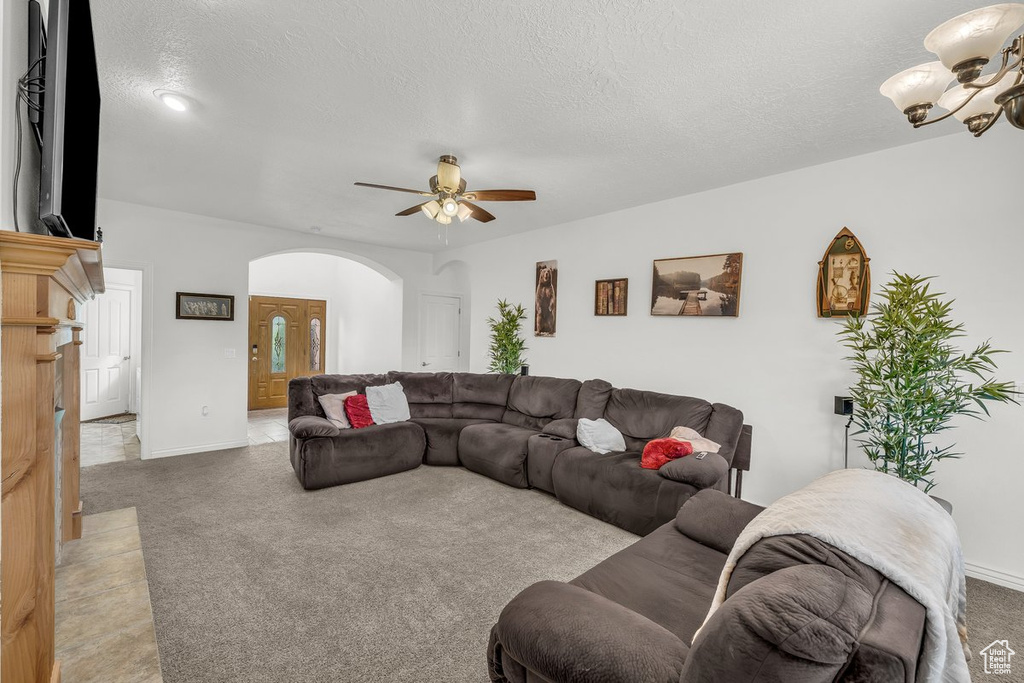 Carpeted living area featuring arched walkways, a ceiling fan, a chandelier, a textured ceiling, and baseboards