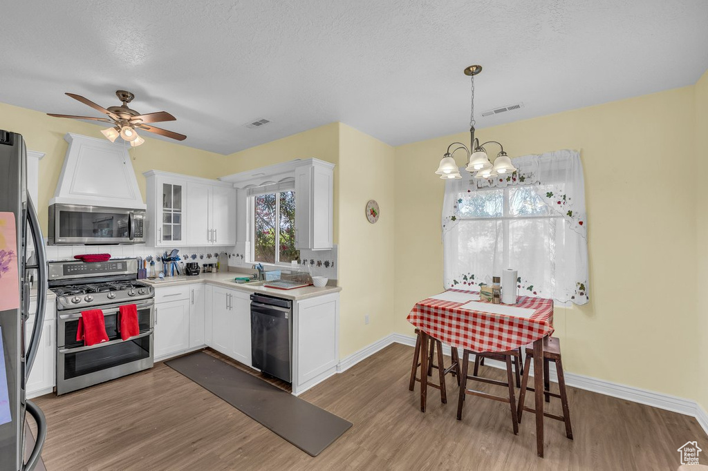 Kitchen featuring stainless steel appliances, white cabinets, wood finished floors, a chandelier, and light countertops