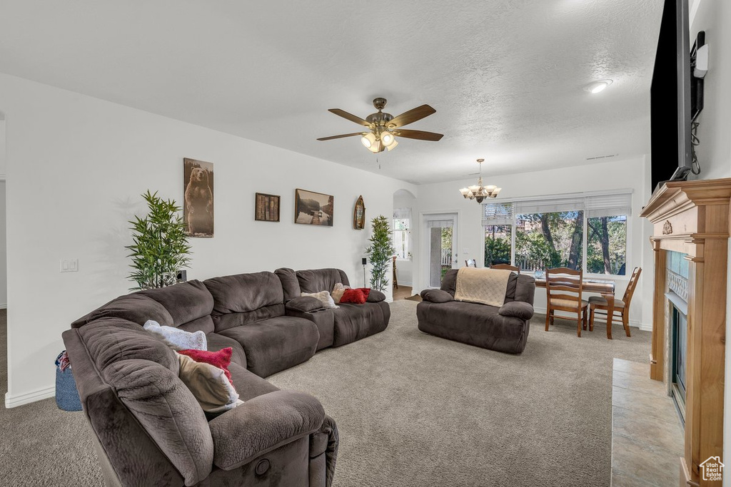 Living area with a chandelier, ceiling fan, a fireplace with flush hearth, light colored carpet, and a textured ceiling