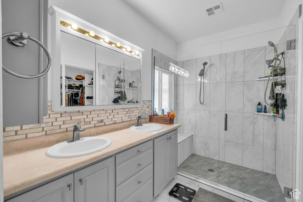 Bathroom featuring a shower stall, backsplash, double vanity, a walk in closet, and tile patterned floors