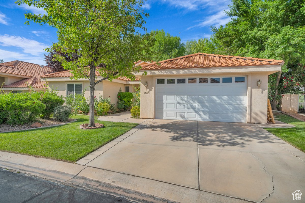 Mediterranean / spanish house featuring stucco siding, a tile roof, a front yard, and a garage