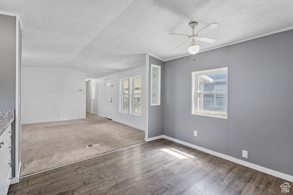 Empty room with ceiling fan, wood finished floors, baseboards, vaulted ceiling, and a textured ceiling