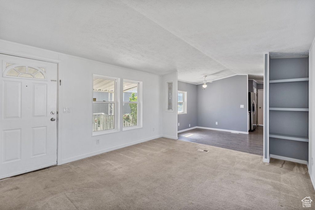 Unfurnished living room with carpet floors, baseboards, a textured ceiling, and vaulted ceiling