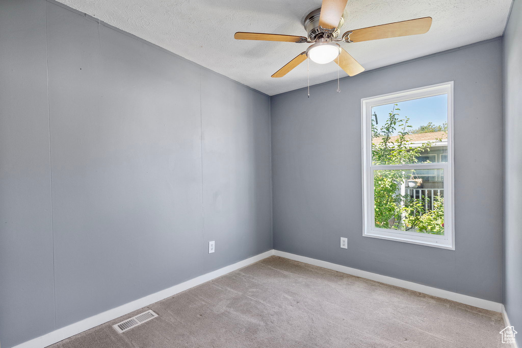 Carpeted empty room with a ceiling fan, baseboards, and a textured ceiling