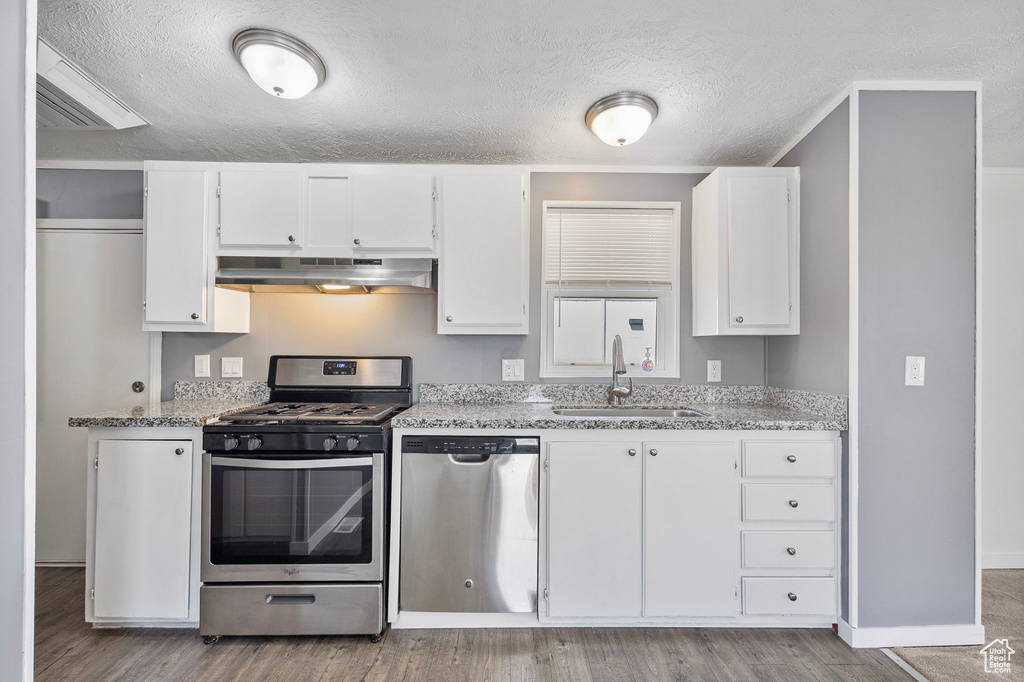 Kitchen featuring stainless steel appliances, a sink, extractor fan, white cabinetry, and wood finished floors