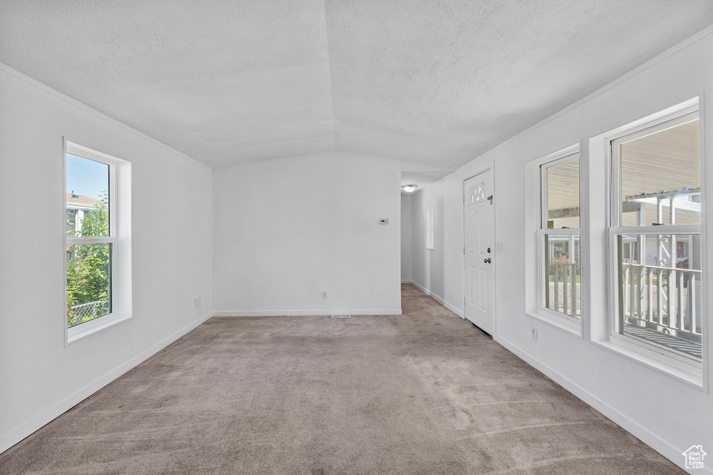 Carpeted spare room with a textured ceiling, vaulted ceiling, and baseboards