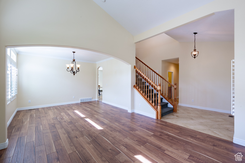 Unfurnished living room with arched walkways, a chandelier, wood finished floors, stairs, and high vaulted ceiling