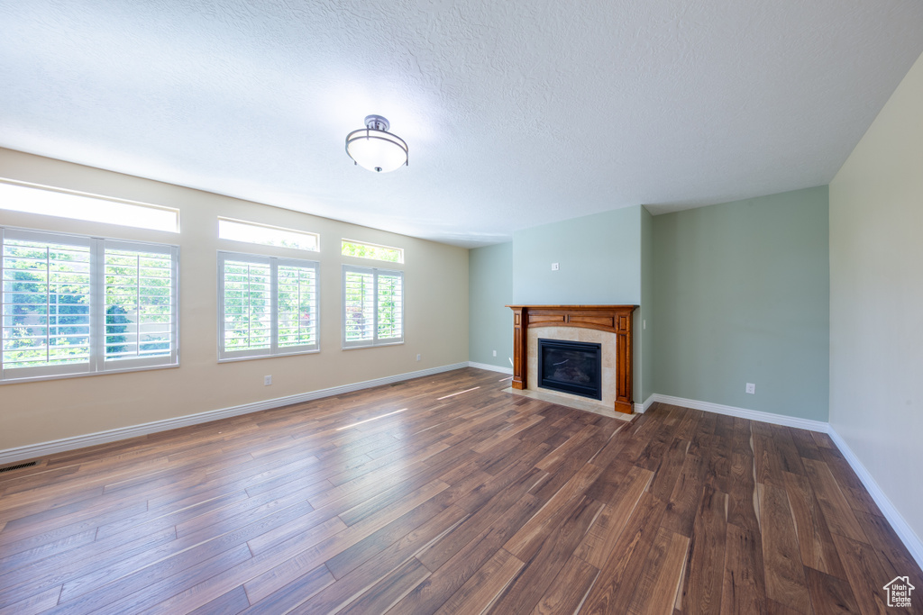 Unfurnished living room featuring dark wood finished floors, a tiled fireplace, baseboards, and a textured ceiling