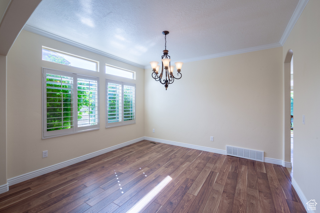 Unfurnished room featuring arched walkways, wood finished floors, crown molding, healthy amount of natural light, and a chandelier