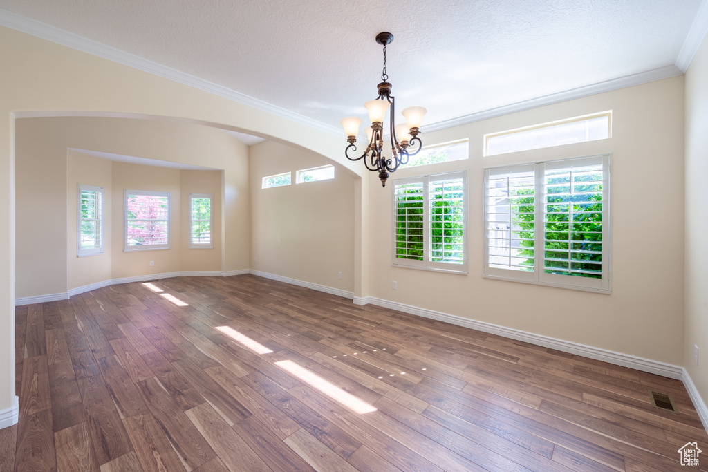 Unfurnished room with a chandelier, ornamental molding, dark wood-style flooring, baseboards, and arched walkways