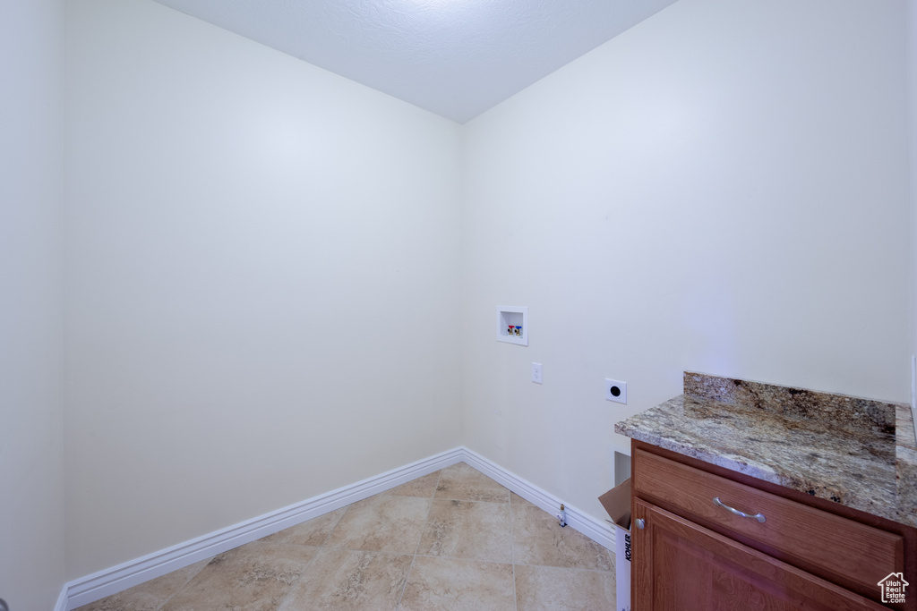 Laundry room with electric dryer hookup, hookup for a washing machine, baseboards, cabinet space, and light tile patterned floors