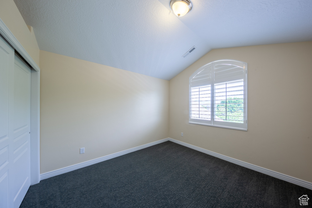 Unfurnished bedroom featuring lofted ceiling, dark carpet, a closet, and baseboards
