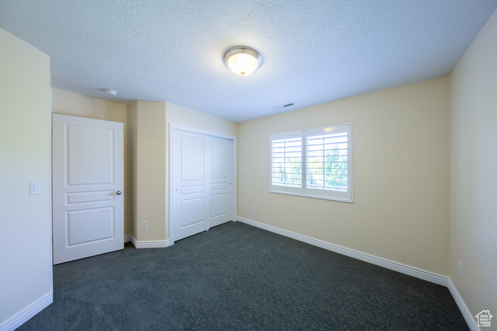 Unfurnished bedroom with dark colored carpet, a closet, a textured ceiling, and baseboards