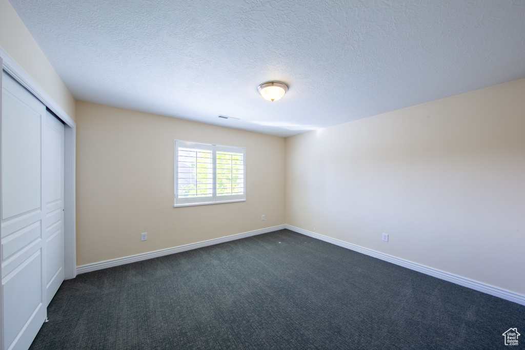Unfurnished bedroom with dark carpet, a closet, baseboards, and a textured ceiling