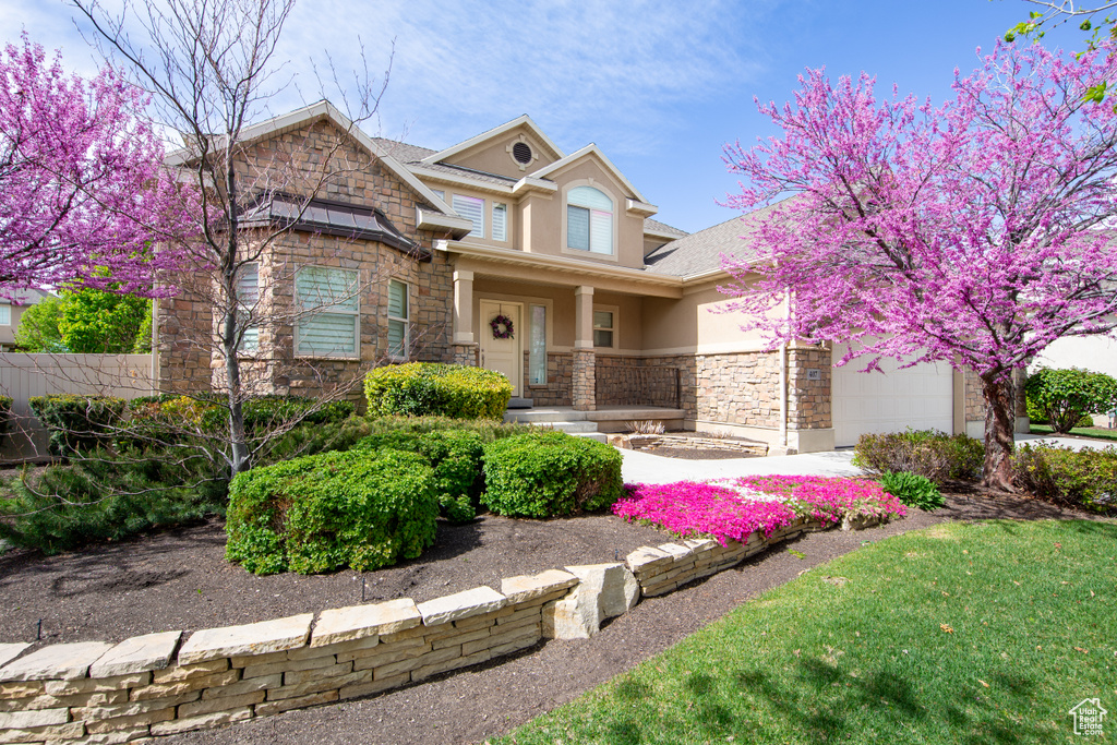 View of front facade featuring stone siding, stucco siding, a garage, and a porch
