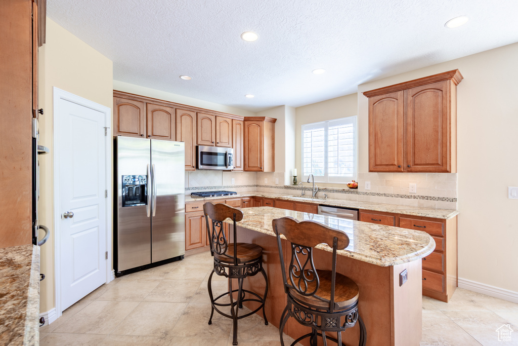 Kitchen featuring stainless steel appliances, a sink, a kitchen bar, light stone counters, and a kitchen island