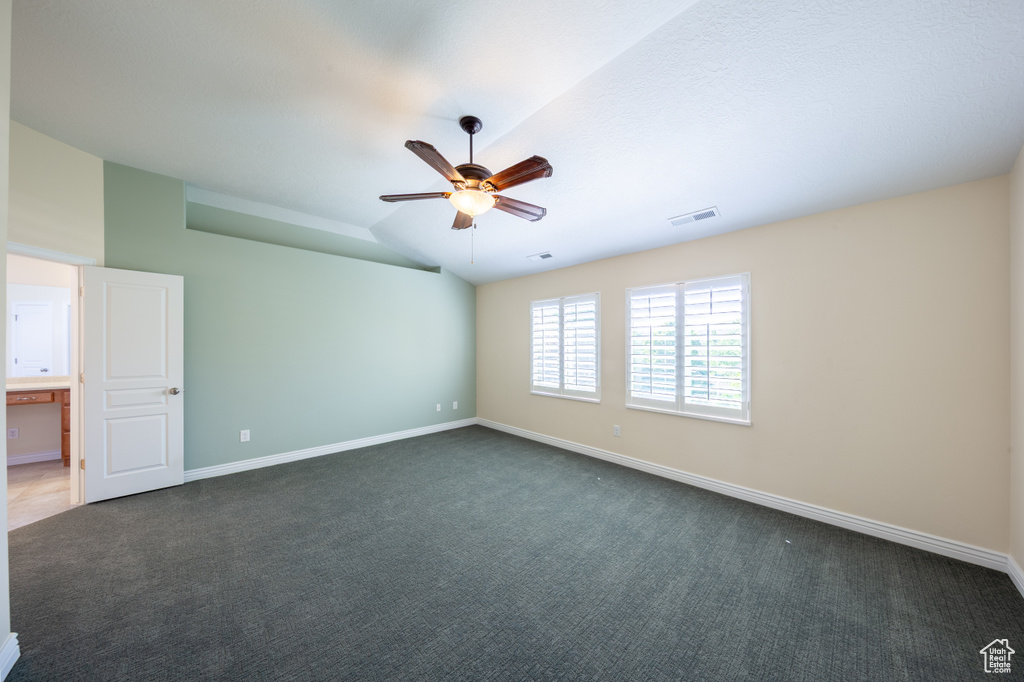 Unfurnished room featuring dark carpet, ceiling fan, baseboards, and lofted ceiling