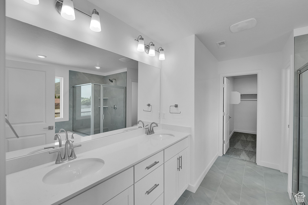 Bathroom featuring a shower stall, double vanity, a spacious closet, baseboards, and recessed lighting