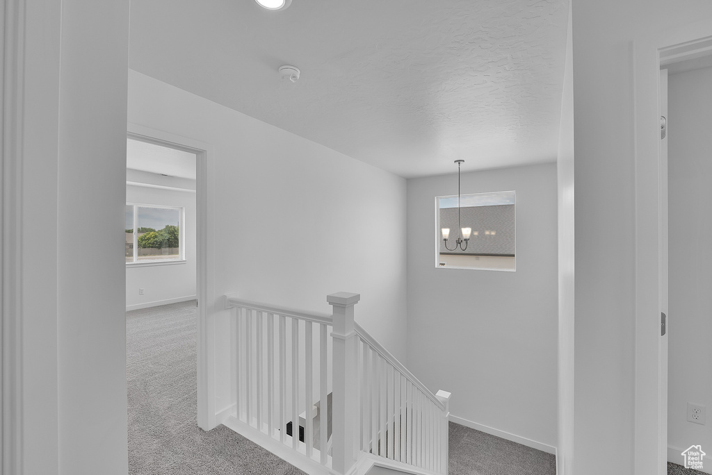 Corridor with an upstairs landing, carpet, a chandelier, and baseboards