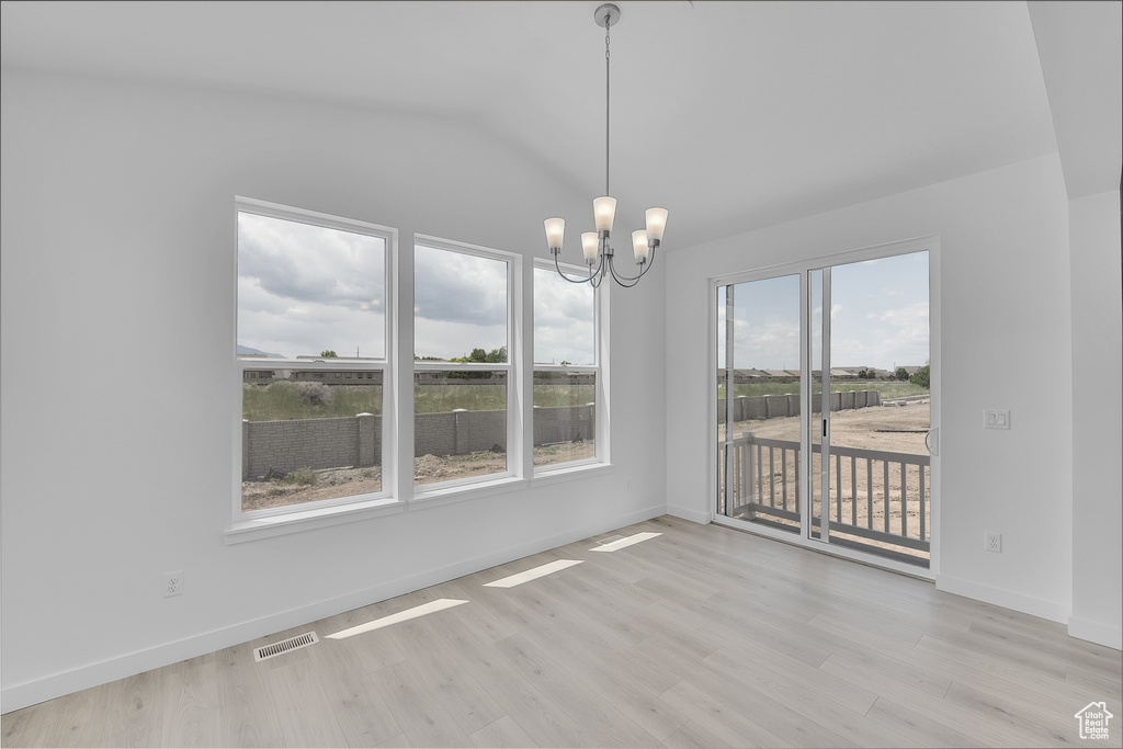 Unfurnished dining area with a chandelier, vaulted ceiling, light wood-style flooring, and baseboards