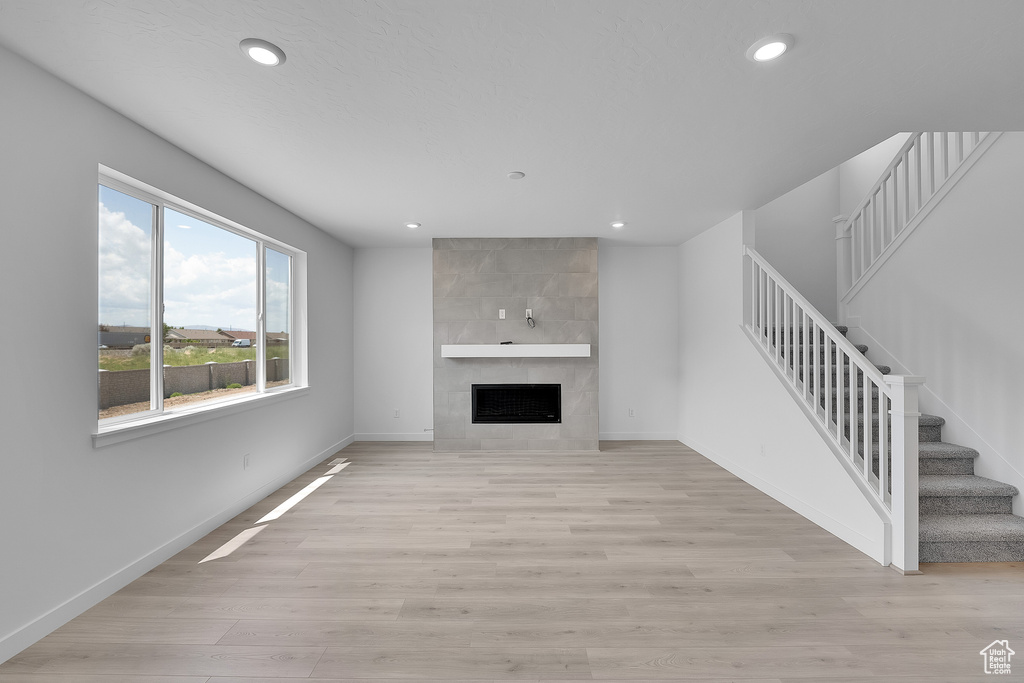 Unfurnished living room with recessed lighting, stairs, baseboards, light wood-style flooring, and a tiled fireplace
