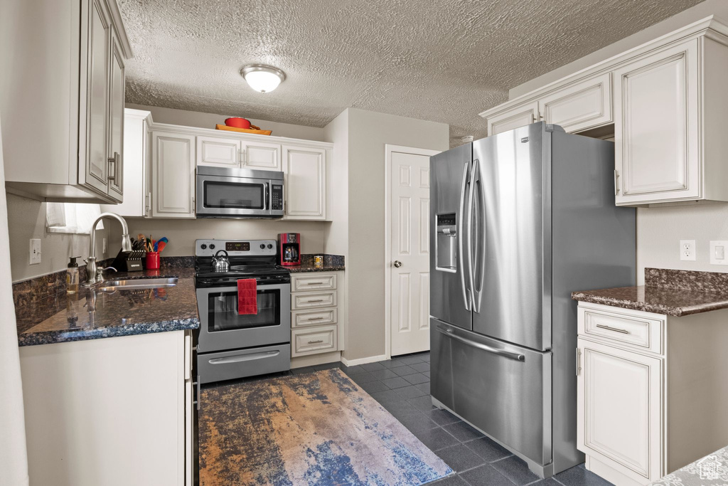 Kitchen with appliances with stainless steel finishes, a sink, dark tile patterned flooring, white cabinets, and a textured ceiling