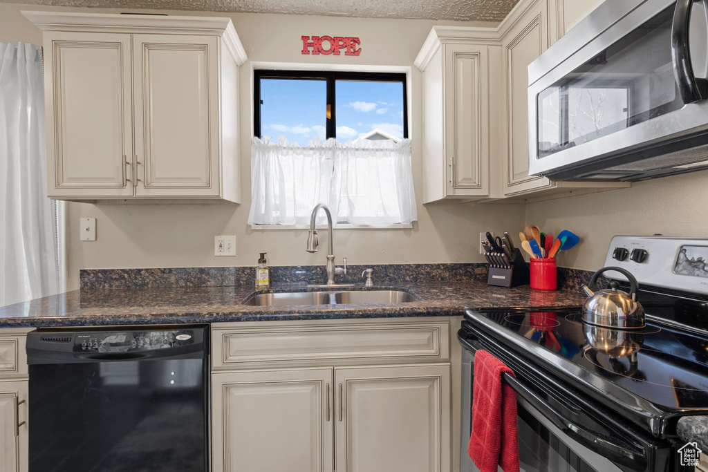 Kitchen with appliances with stainless steel finishes, a sink, and dark stone counters