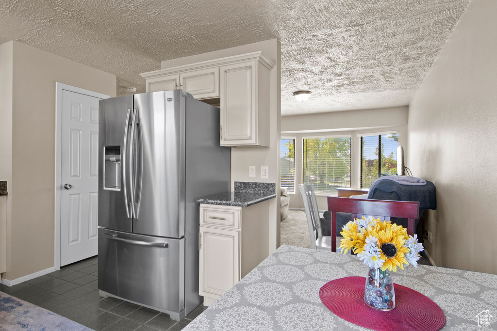 Kitchen featuring stainless steel fridge, a textured ceiling, dark tile patterned floors, white cabinetry, and baseboards