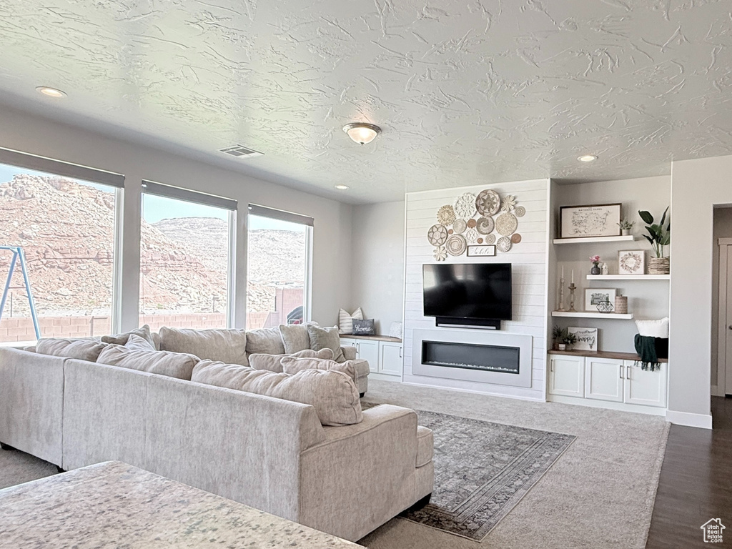 Living room with baseboards, recessed lighting, dark wood-type flooring, a textured ceiling, and a fireplace