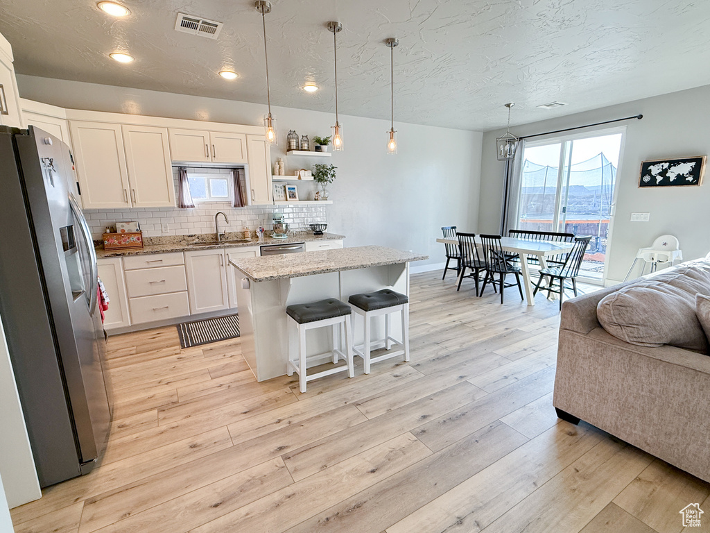 Kitchen featuring appliances with stainless steel finishes, a textured ceiling, white cabinets, light stone countertops, and a kitchen island